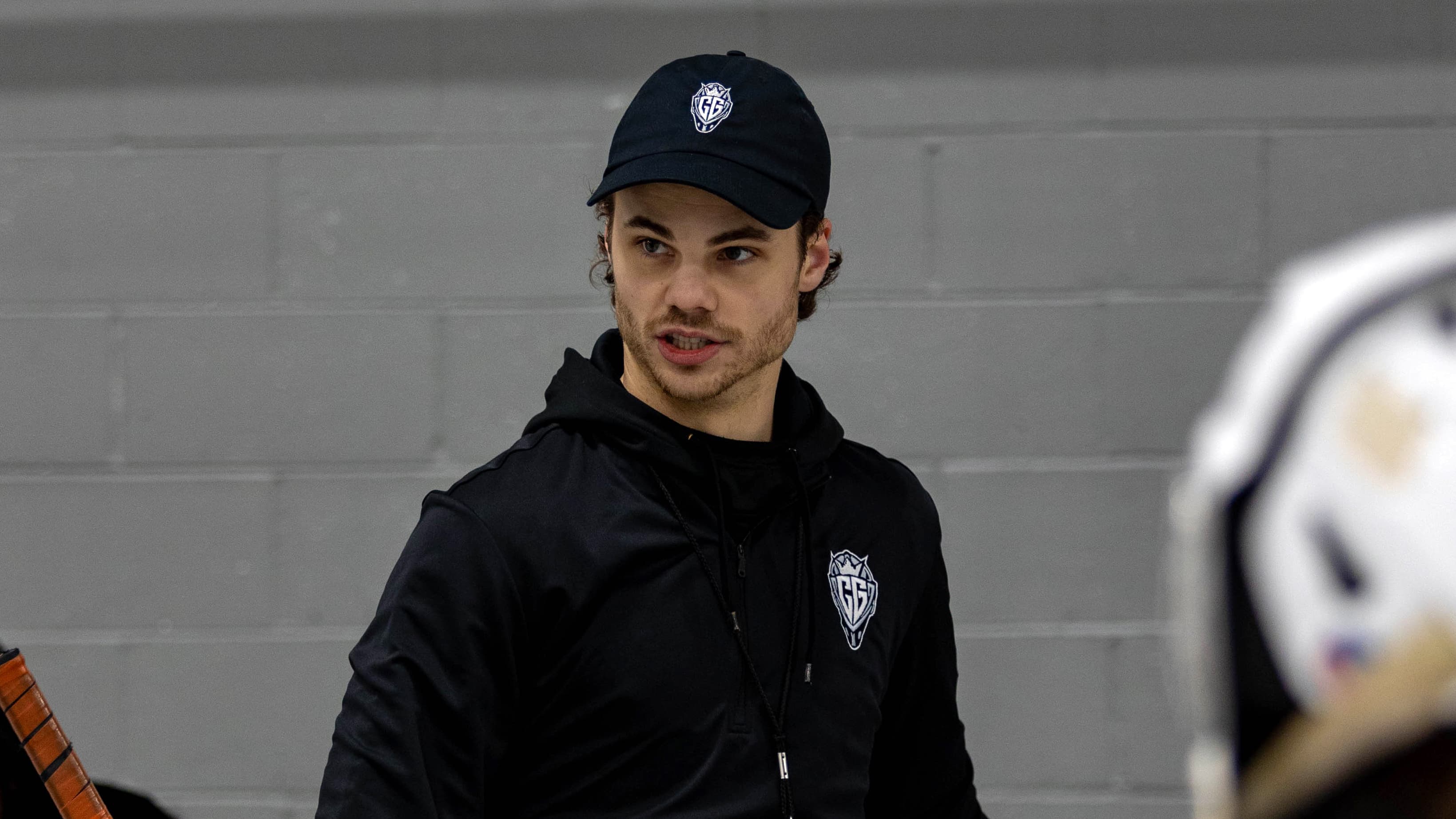 Cam Gray in a CGG cap and hoodie, mid-conversation rinkside.